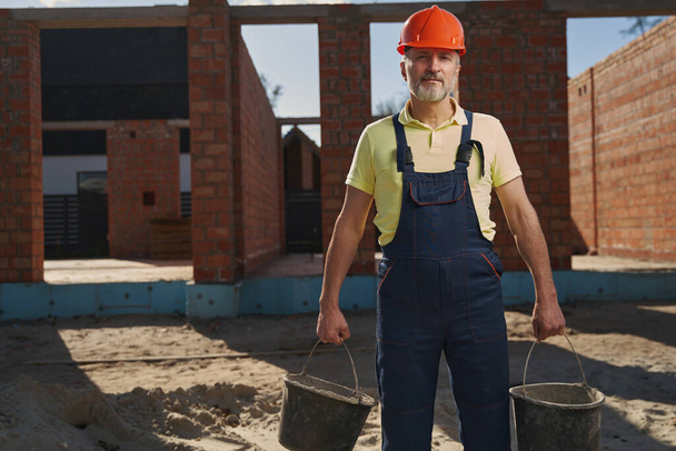 Male housebuilder with two buckets looking at camera - Фото, зображення
