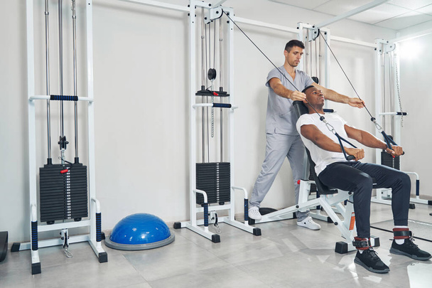 Man performing seated straight-arm pulldown aided by kinesiologist - Foto, Bild