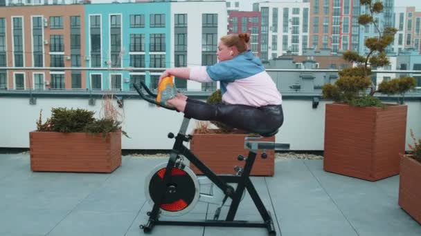 Кавказская женщина-тренер делает упражнения по аэробике на стационарном велосипеде на открытом воздухе - Кадры, видео