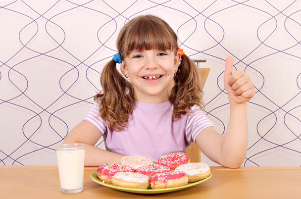 親指アップと朝食にドーナツとの幸せな女の子 - 写真・画像