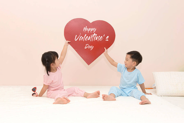 happy little Asian boy and girl with a red heart over pink background. valentines day concept  - Fotó, kép