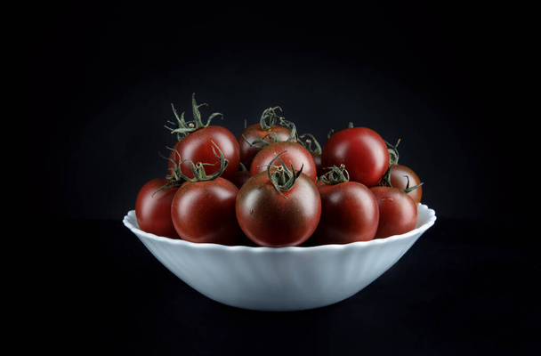 Beautiful tomatoes in a white plate on a black background. Cumato tomatoes. - Photo, Image