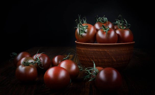 Ripe juicy tomatoes in a clay plate and next to it on a black background. - Fotoğraf, Görsel