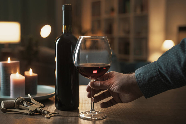 Man drinking a glass or red wine at home, room interior in the background - Foto, afbeelding