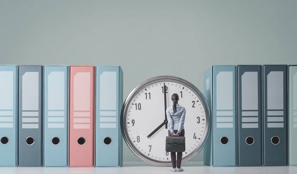 Businesswoman holding her briefcase and checking the time on a huge clock, she is standing and waiting - Фото, изображение