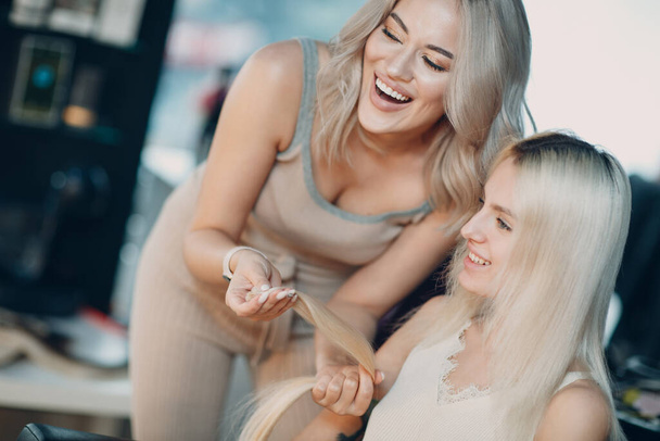 Coiffeur femelle faire des extensions de cheveux à la jeune femme aux cheveux blonds dans le salon de beauté. Extension de cheveux professionnelle. - Photo, image