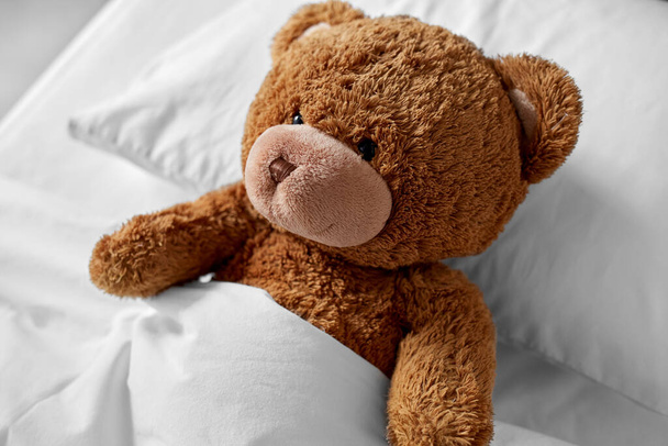 teddy beer speelgoed liggend bedekt met deken in bed - Foto, afbeelding