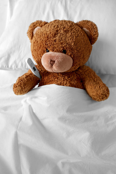 ill teddy bear toy head with thermometer in bed - Фото, изображение