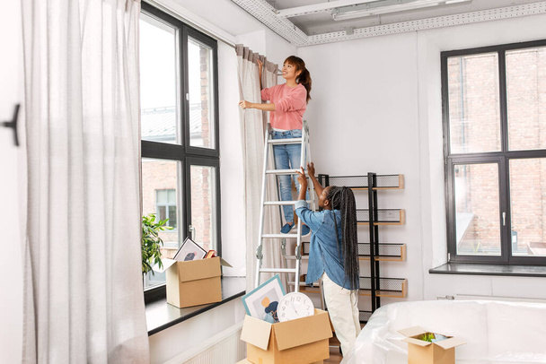 woman on ladder hanging curtains at home - Фото, зображення