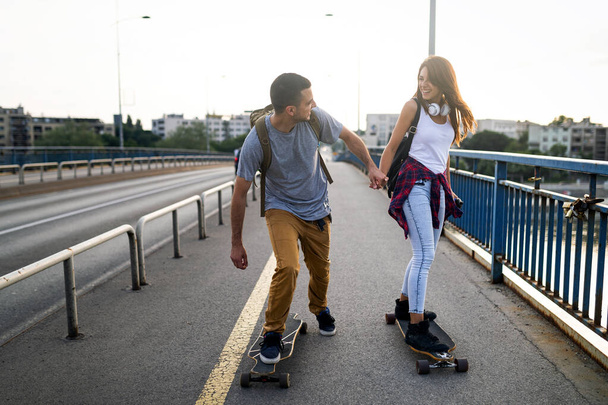 Portrait of happy couple having fun while driving a long board in city outdoors. People skateboard concept - Fotó, kép