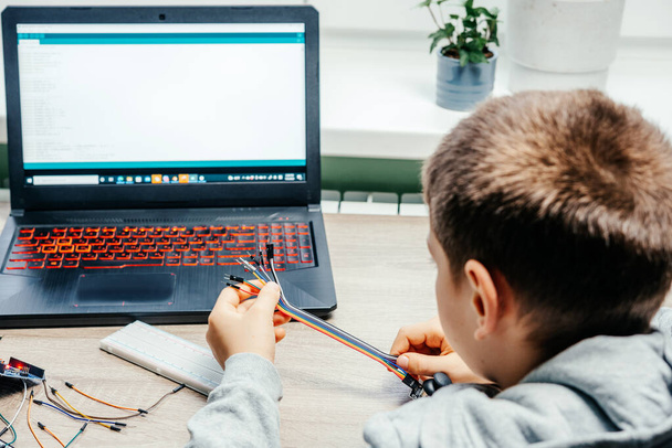 Egy fiú bedugja a kábeleket az érzékelőchipekbe, miközben arduino kódolást és robotikát tanul. - Fotó, kép