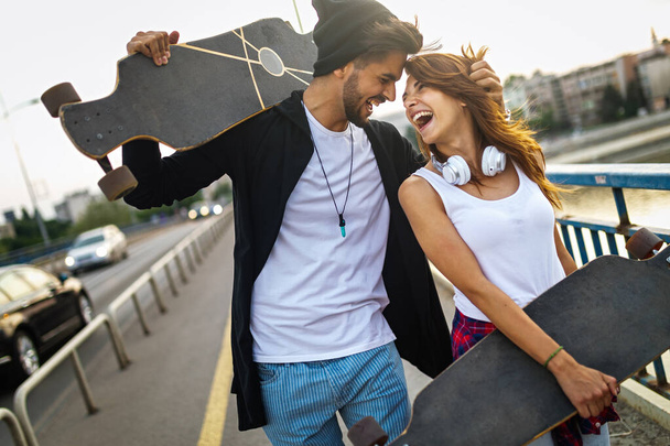 Retrato de pareja feliz joven con patinetas divirtiéndose juntos al aire libre - Foto, imagen