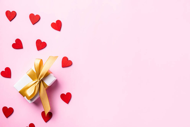 Happy Valentines' day background concept. White gift box with a golden bow ribbon and wood red hearts composition for love isolated on pink background with copy space. Top View from above - Φωτογραφία, εικόνα
