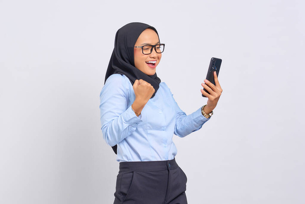 Portrait of excited young Asian woman celebrating with mobile phone isolated on white background - Foto, afbeelding