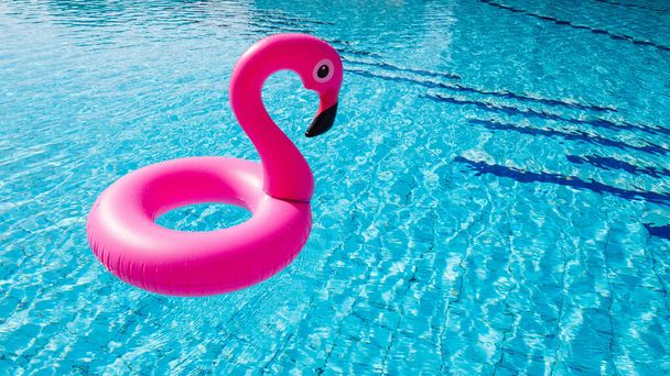 Różowy basen. Różowy dmuchany flaming w wodzie na letnie tło plaży. Zabawna zabawka dla dzieci - Zdjęcie, obraz