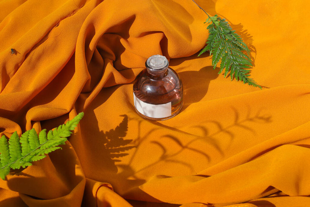 Frasco de perfume de 50 ml com rótulo branco em branco e folhas verdes sobre fundo tecido laranja texturizado. Frasco de perfume foto stock - Foto, Imagem