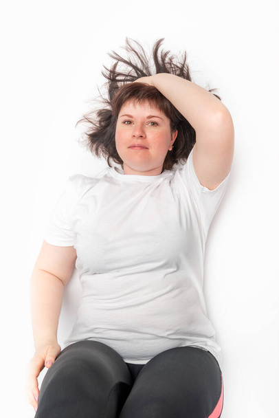 Young plump woman is tired after playing sports. Top view portrait of chubby girl on white background - Foto, afbeelding