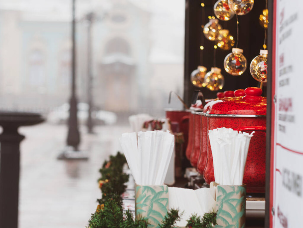 Rode potten met glühwein op kerstmarkt verlicht kraam. Seizoensgebonden vakantie straat voedsel dranken concept. Heerlijke warme wijn geurige kruiden te koop op het stadsplein. Nieuwjaar warme dranken winter tijd - Foto, afbeelding