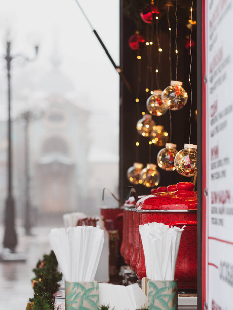 Rote Töpfe mit Glühwein auf dem Weihnachtsmarkt beleuchteten Stand. Das Konzept der saisonalen Streetfood-Getränke für den Urlaub. Leckerer Glühwein- und Gewürzverkauf auf dem Stadtplatz. Heißgetränke zum Jahreswechsel Winterzeit - Foto, Bild