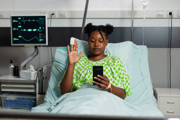 Africano americano doente mulher segurando smarphone cumprimentando amigos remotos explicando tratamento médico - Foto, Imagem