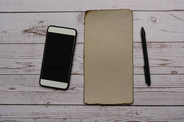 Burnt edge brown paper with pen and smartphone on wooden desk. Blank for text - Foto, Imagem