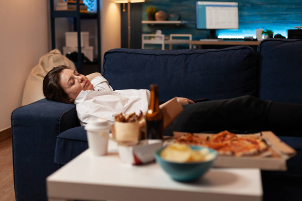 Κουρασμένη γυναίκα κοιμάται καναπέ μετά από μεγάλο fast food takeaway δείπνο μπροστά στην τηλεόραση - Φωτογραφία, εικόνα