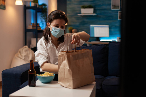 Caucasian female back from office with face mask preparing to unpack takeaway bag - 写真・画像