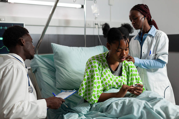 Хворий пацієнт стоїть в ліжку, афроамериканський лікар спостерігає за частотою серцевих скорочень
 - Фото, зображення