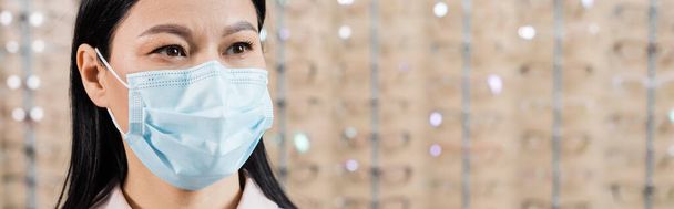 asian ophthalmologist in medical mask in optics salon on blurred background, banner - Foto, imagen