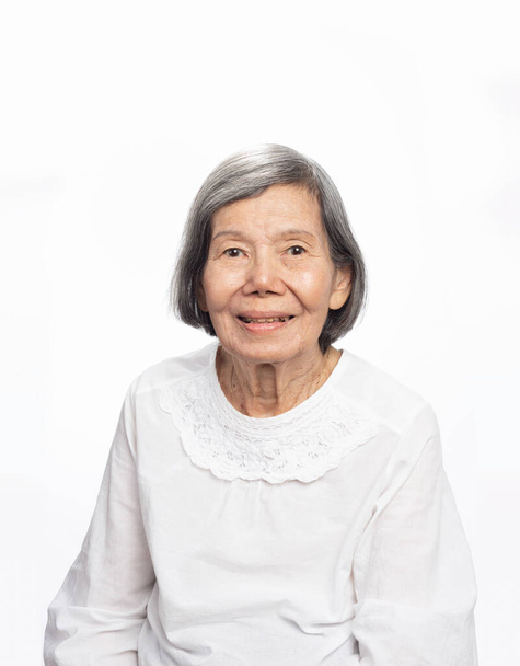 Portrait d'une mignonne femme asiatique âgée souriante des années 80 regardant la caméra isolée sur blanc. Mature vieille dame gros plan portrait. - Photo, image