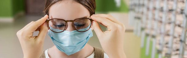 oculist putting eyeglasses on girl in medical mask, banner - Zdjęcie, obraz