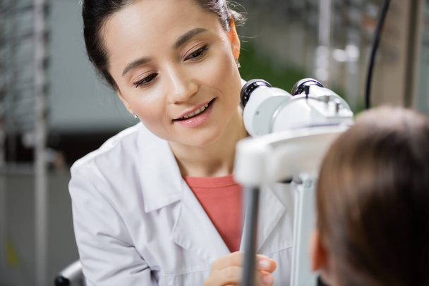 positive optometrist checking eyesight of girl on autorefractor in optics store - Photo, Image