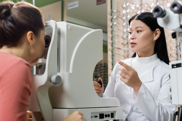 азіатський окуліст вказує пальцем при вимірюванні зір розмитої жінки на екрані зору
 - Фото, зображення