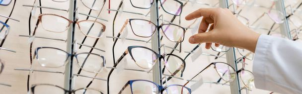 cropped view of oculist taking eyeglasses in optics store, banner - 写真・画像