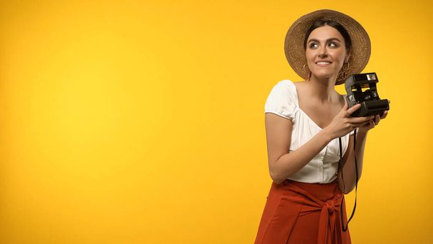 Cheerful tourist in straw hat holding vintage camera isolated on yellow - Photo, Image