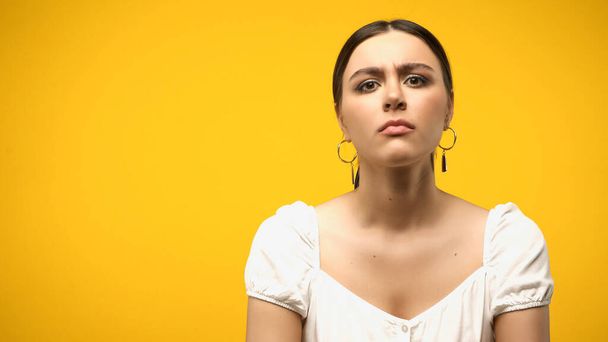 Skeptical woman in blouse and earrings looking at camera isolated on yellow  - Foto, Bild