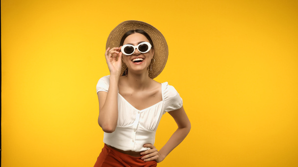 Cheerful woman holding sunglasses and hand on hip isolated on yellow  - Fotografie, Obrázek