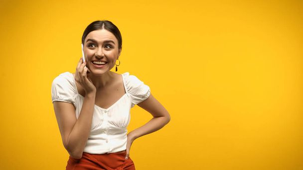 Positive woman talking on mobile phone isolated on yellow  - Foto, Imagem