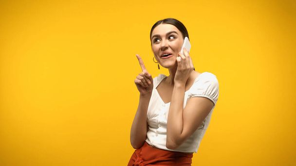 Brunette woman talking on cellphone and having idea isolated on yellow  - Foto, Imagen