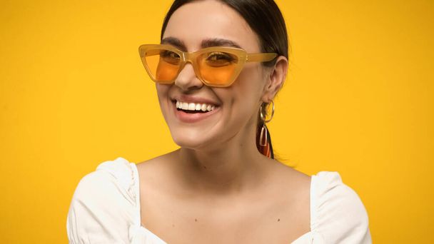 Smiling model in sunglasses and blouse looking at camera isolated on yellow - Foto, immagini