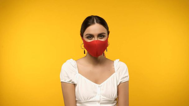 Fiatal nő védő maszkban nézi kamera elszigetelt sárga - Fotó, kép