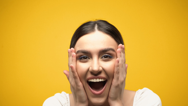 Excited brunette model touching cheeks isolated on yellow  - Valokuva, kuva