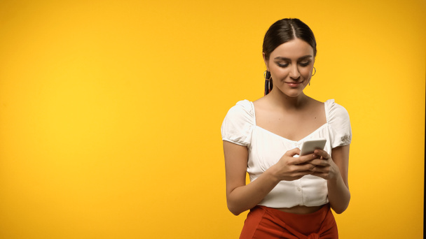 Smiling woman in blouse using cellphone isolated on yellow  - Foto, Imagem