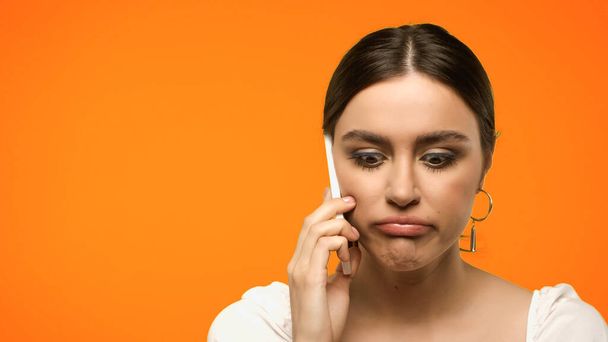 Displeased brunette woman talking on smartphone isolated on orange  - Фото, изображение
