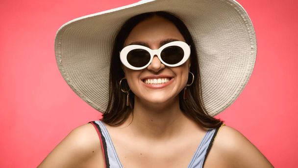 Smiling brunette woman in sunglasses and swimsuit posing isolated on pink  - Foto, Imagen