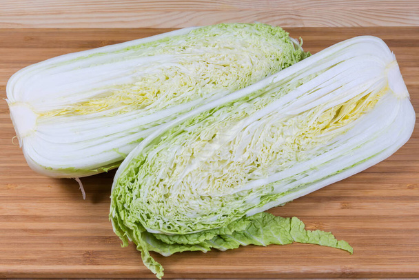 Two halves of head of napa cabbage, or chinese cabbage, cut lengthwise lie on a wooden cutting board - Fotó, kép