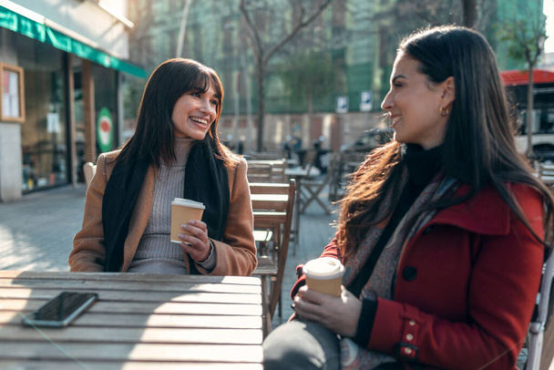 Shot of two attractive friends enjoying coffee together while talking and laughing sitting on the terrace of a bar. - Foto, Imagem