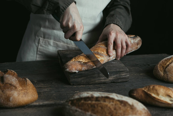 Las manos femeninas están cortando pan de centeno. Pan sin levadura. Concepto de comida saludable y horneado tradicional. Foto de alta calidad - Foto, Imagen
