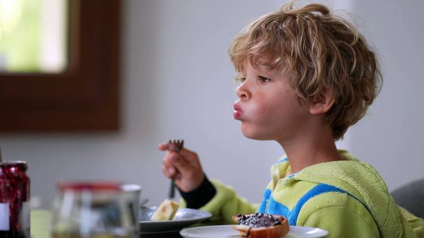 Pensive child sitting at breakfast table eating fruit. thoughtful boy - Foto, afbeelding