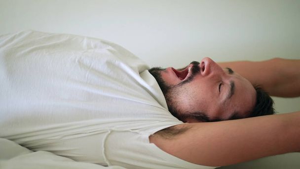 Ο άντρας που χασμουριέται ξυπνάει από τον ύπνο, το άτομο που ξαπλώνει στο κρεβάτι χασμουριέται - Φωτογραφία, εικόνα